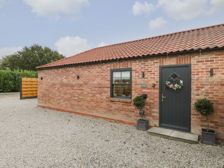 The exterior of a brick building with a tiled roof a black door with a wreath two potted plants and a gravel ground at Bracken Cottage in Pocklington