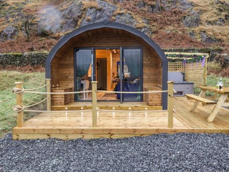 A wooden pod with glass double doors opening onto a wooden deck with rope railings and a picnic table at The Shearer - Crossgate Luxury Glamping Hartsop near Glenridding