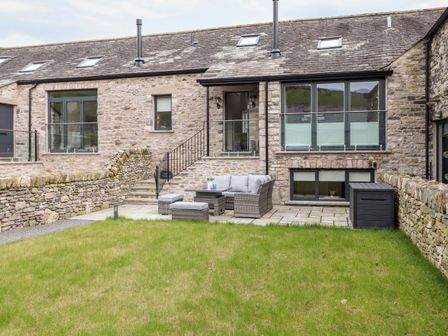 A stone house with outdoor seating on a patio and a grassy lawn at Ada's Hideaway in Stainton near Sizergh Cumbria