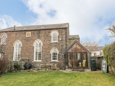 A stone house with arched windows a glass porch table and chairs on the lawn at 2 The Reformed Church in Embleton