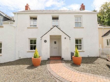 A white two-story house with a central door and four windows with a brick pathway and two large plant pots at The Old Farm House in Redberth near Pentlepoir