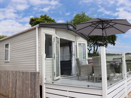 A mobile home with open doors leading to a patio with wicker chairs and a large umbrella at The Retreat in Otterton
