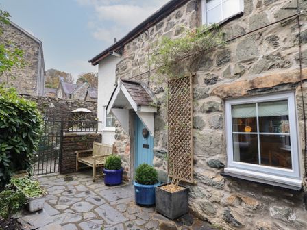 An outdoor stone patio with a wooden bench blue door and potted plants at 3 Ivy Court in Dolgellau