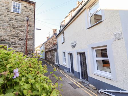 A narrow street with stone and white buildings and green plants in the foreground at Deu-Ddrws in Barmouth