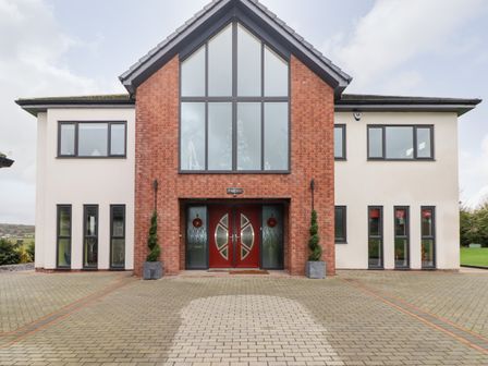 Front view of a modern two-story house with large windows and a red double door at Ty Marlyn in Crofty