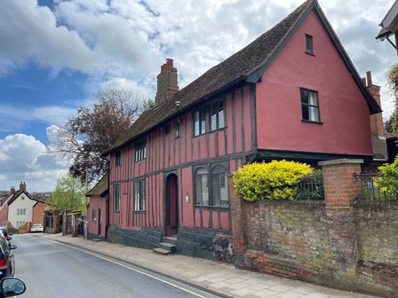A street with a timber framed house painted red with black beams and a brick wall with yellow bushes at The Bridewell in Woodbridge