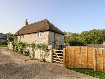 A stone house with a thatched roof and a wooden fence around the property at Dairy Cottage in Abbotsbury
