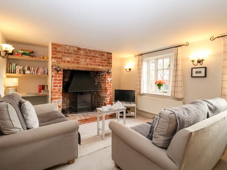 A living room with sofas around a brick fireplace and a small table with a tea set at 2 Mosses Cottage in Friston