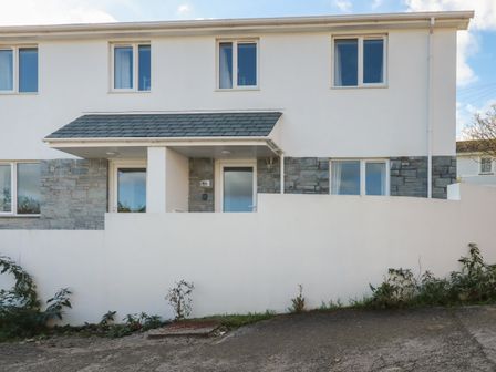 A two story house with white walls stone accents and a small porch at 6A The Mews in Harlyn Bay Cornwall
