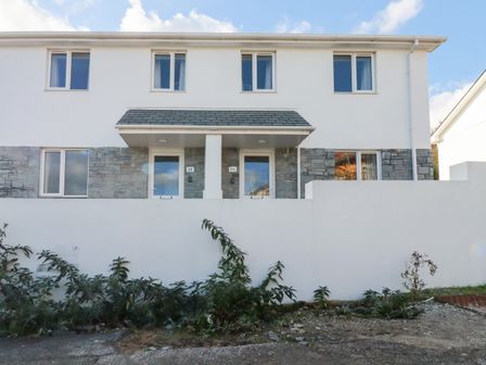 Exterior of a two-story semi-detached house with white walls stone accents and a low white front wall at 6B The Mews Harlyn Bay Cornwall