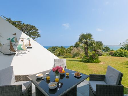 An outdoor patio with a glass table and four chairs overlooking a garden and the sea at Millies in Carbis Bay