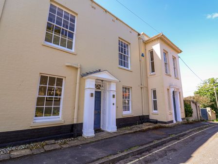 A street view of light yellow brick houses with blue doors and white window frames at The Middle House in Southwold