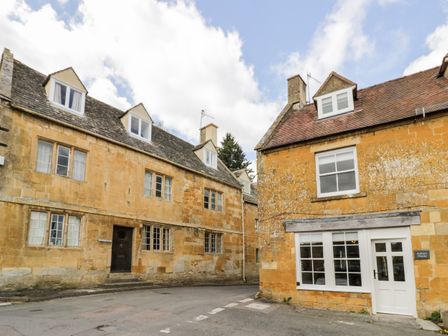 A street view of stone buildings with windows and a white door at Ashton House in Blockley