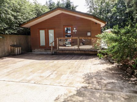 A wooden cabin with a small porch and glass railing in a wooded area at Washburn Lodge in Fewston near Darley