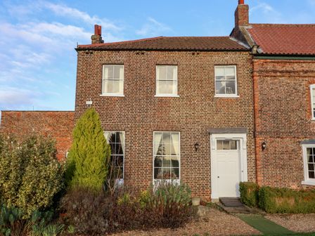 A brick house with white door and windows surrounded by shrubs and bushes at The Stables and West Wing Bolton Percy near Tadcaster