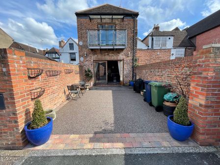 A brick courtyard with a small balcony a table and chairs and trash bins at The Coach House in Tewkesbury