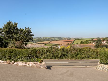 A country road with hedges and houses with tiled roofs with fields and hills in the background at Thornberry in Salcombe