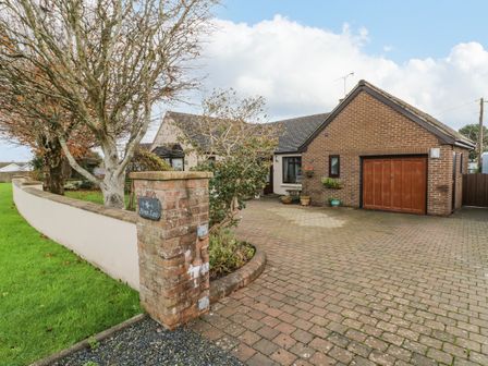A brick and stucco house with a garage and a paved driveway with trees and a low wall at Penn Lea in Penally