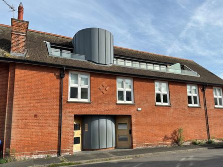Brick building with multiple white windows wooden doors and a rounded metal structure on the roof at The Old Gymnasium in Southwold