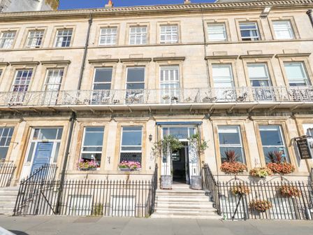 A stone building facade with multiple windows flower boxes and a wrought iron fence at The Esplanade in Weymouth