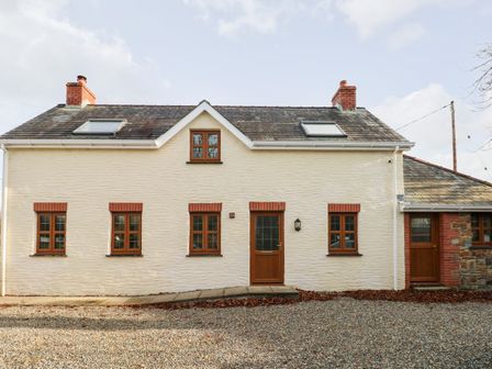 A front view of a two chimney cottage with multiple windows and two wooden doors at Ty Melyn in Boncath