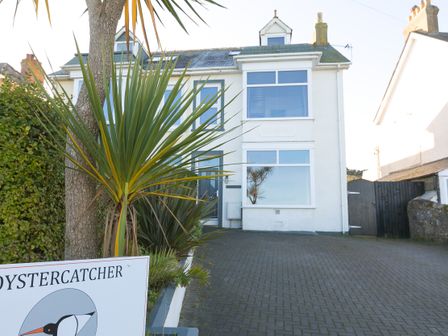 A white two-story house with large windows and a paved driveway with plants in front at Oystercatcher House in Carbis Bay