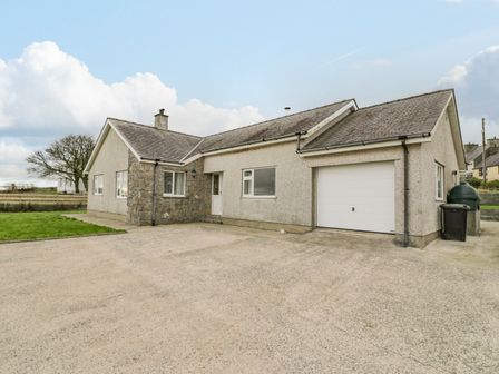 A single story house with a paved driveway and a garage door at Cynefin in Pencraigwen near Dulas