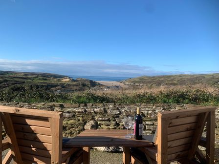 Two wooden chairs and a table with a bottle of wine and two glasses overlooking a stone wall and coastal landscape at Little Seacroft in Crantock