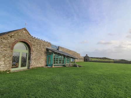 A stone building with green doors and windows next to a large green lawn at Lower Treginnis Farm in St Davids