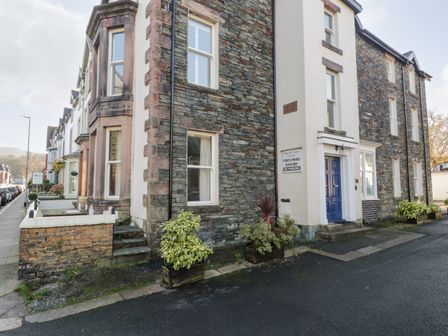 The exterior of a stone building with windows and a blue door next to a sidewalk with parked cars at Carlton House Apartment 1 in Keswick