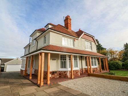 A two story house with a tiled roof wooden porch columns and a driveway at Westholme Lodge in Minehead
