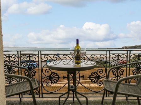 A balcony with a round table holding a bottle and two wine glasses with two chairs and a sea view at Sunbeach in Weymouth