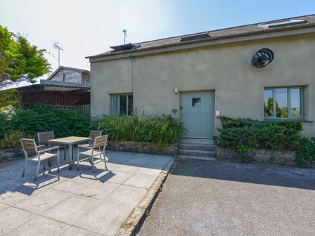 An outdoor patio with a table and four chairs in front of a building with a green door and two windows at Oak Leaves Cottage in Teigngrace near Newton Abbot