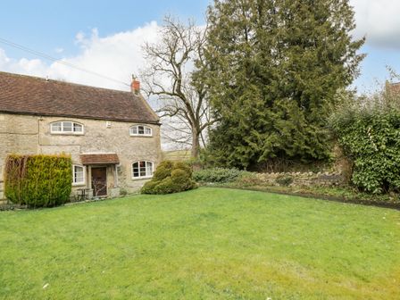 A stone cottage with a tiled roof surrounded by lawn and trees at Field Cottage in Shepton Mallet