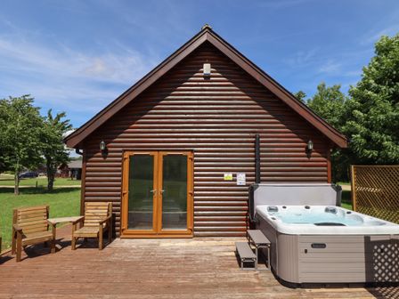 A wooden cabin with glass doors a hot tub and two wooden chairs on a deck at Lodge 1 in South Hykeham