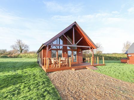 A wooden cabin with a front porch and outdoor furniture surrounded by grass at Lodge 4 in South Hykeham