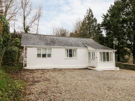 A white single-story house with a gravel driveway and surrounding trees at Priory House Cottage in Barnstaple
