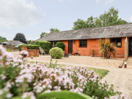 An outdoor area with a brick building and patio furniture surrounded by bushes and flowers at The Granary in Polstead