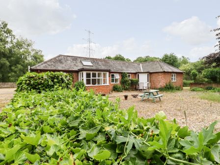 A single-story brick house with a sloped roof and skylight surrounded by greenery and a picnic bench at The Brambles in Polstead