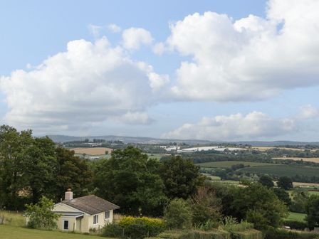 A rural landscape with a small house surrounded by trees and fields under a partly cloudy sky at Palace Bungalow in St Weonards