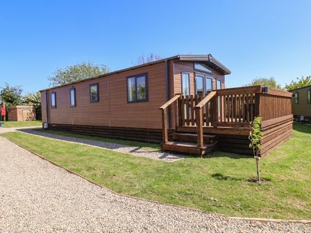 A wooden mobile home with a small deck and stairs surrounded by grass and gravel pathways at Primrose Lodge in Runswick Bay near Staithes