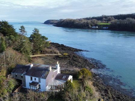 A house near a rocky shoreline with trees and water at Ynys Faelog Cottage in Ynys Faelog near Menai Bridge