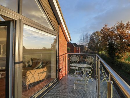 A balcony with metal table and chairs overlooking trees and neighboring houses at Upper Annex in Quemerford