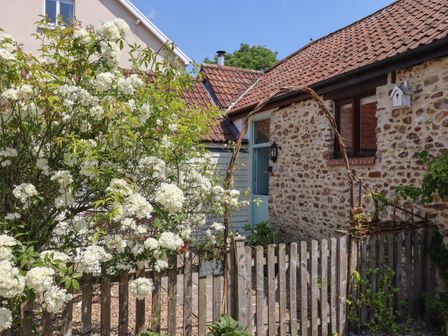 A wooden gate with a flowering bush beside a stone house with a red tile roof at The Bull Pen in Colyton