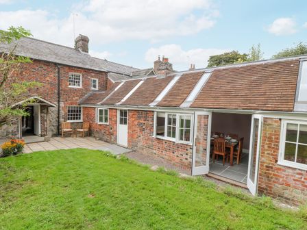 A brick house with a grass lawn and patio chairs outside the door at The Old Bakehouse in Avebury