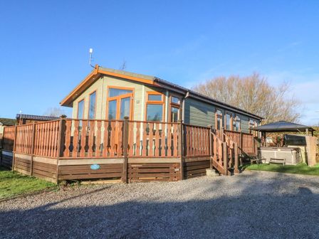 An exterior view of a wooden cabin with a wraparound deck and steps with a gazebo and hot tub in the yard at Dream Catcher Lodge in Carnforth