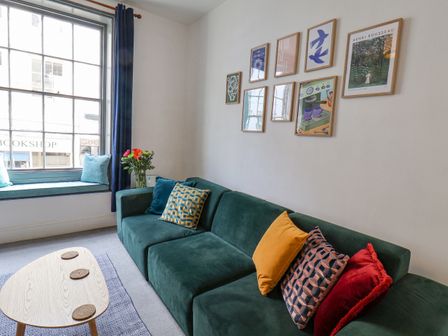 A living room with a green sofa with colorful cushions a wooden coffee table and framed pictures on the wall at Book House in Whitby