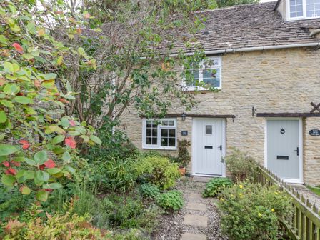 Stone cottage with white doors and windows surrounded by a garden and plants at Thorn Cottage in Fairford
