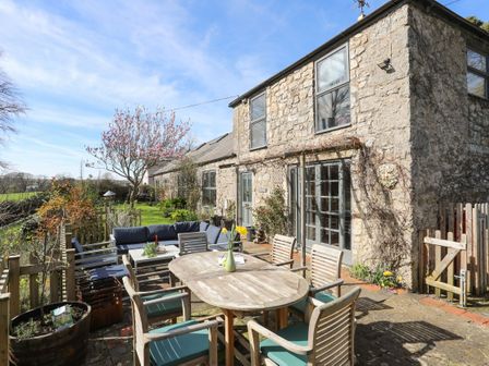 A stone house exterior with a patio table and chairs and a blue cushioned sofa in the garden at Plas Elyn in Llangoed near Beaumaris