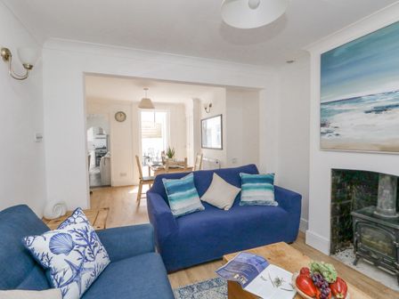A living room with two blue sofas and a wooden coffee table next to a fireplace and dining area in the background at Day Cottage in Weymouth